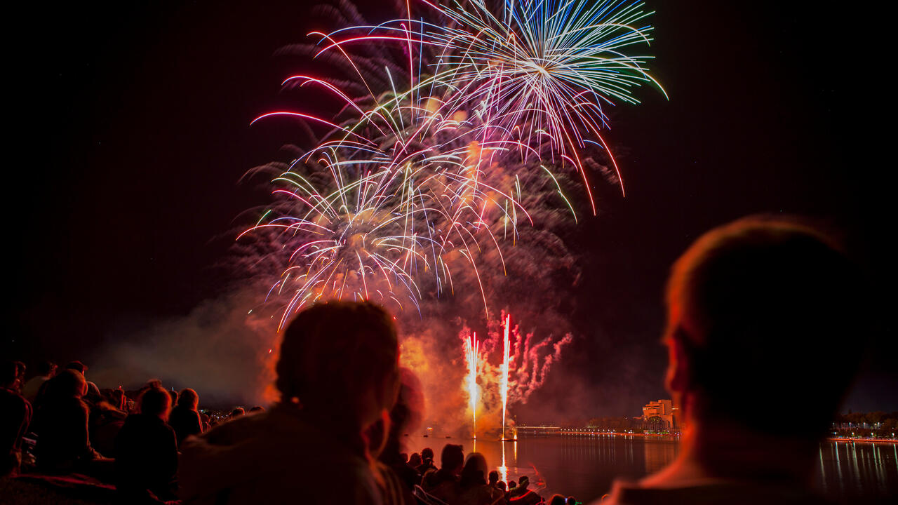 A crowd watches a fireworks display over a lake. 