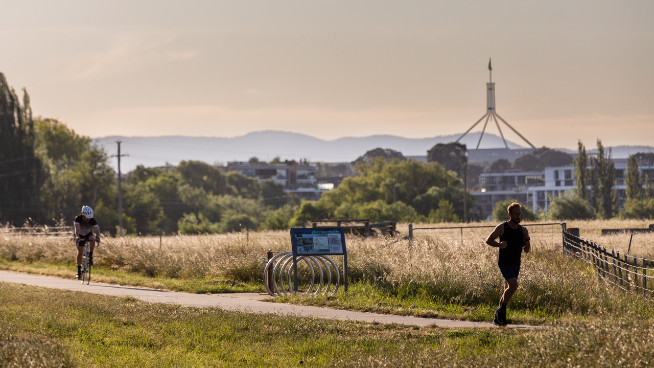 A cyclist and a runner on a track with Parliament House in the background.