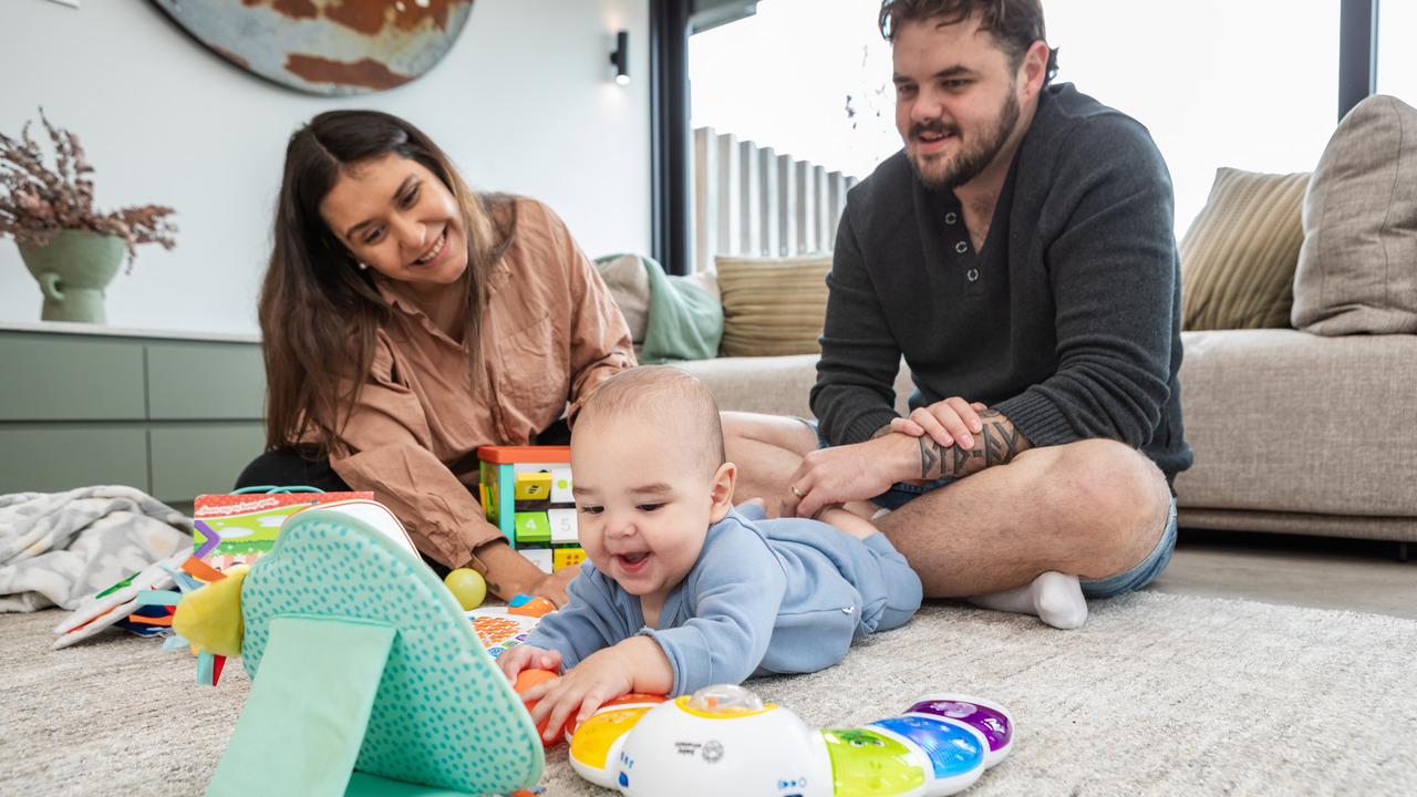 A mother, father and baby sit together on the floor.