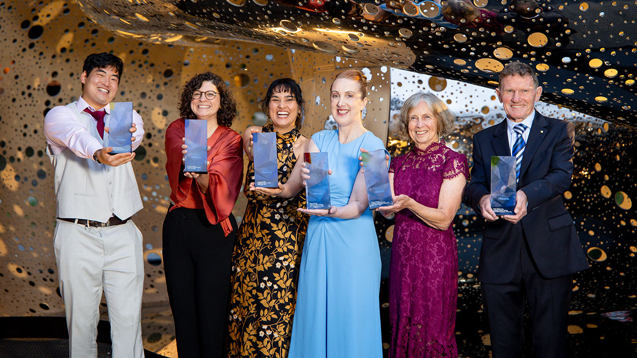 Four women and two men dressed in formal wear smile and hold plaques.