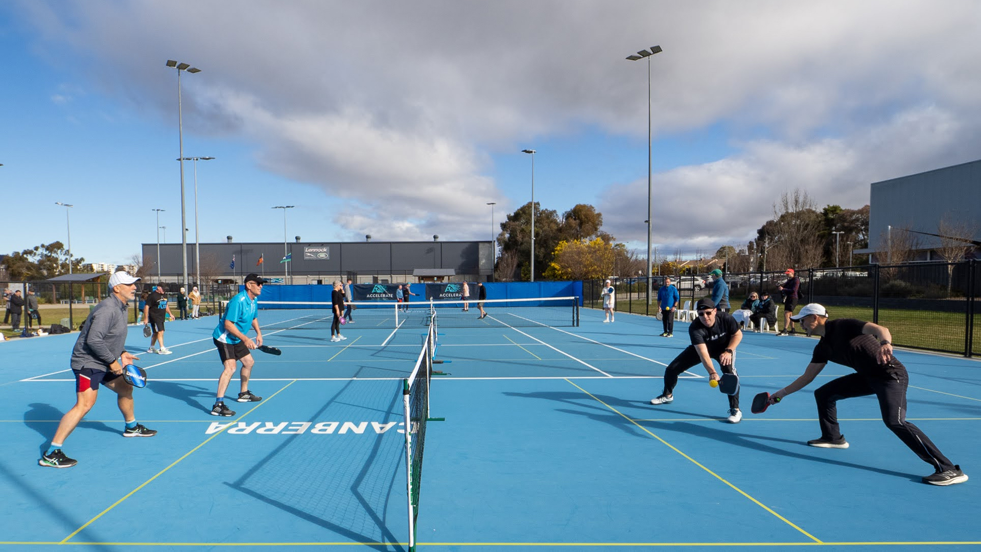 Outdoor courts with people playing a game that looks like tennis but with different bats.