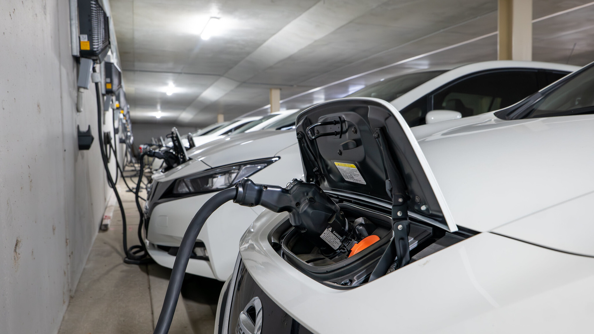 A fleet of electric vehicles are parked and plugged into EV charging bays.
